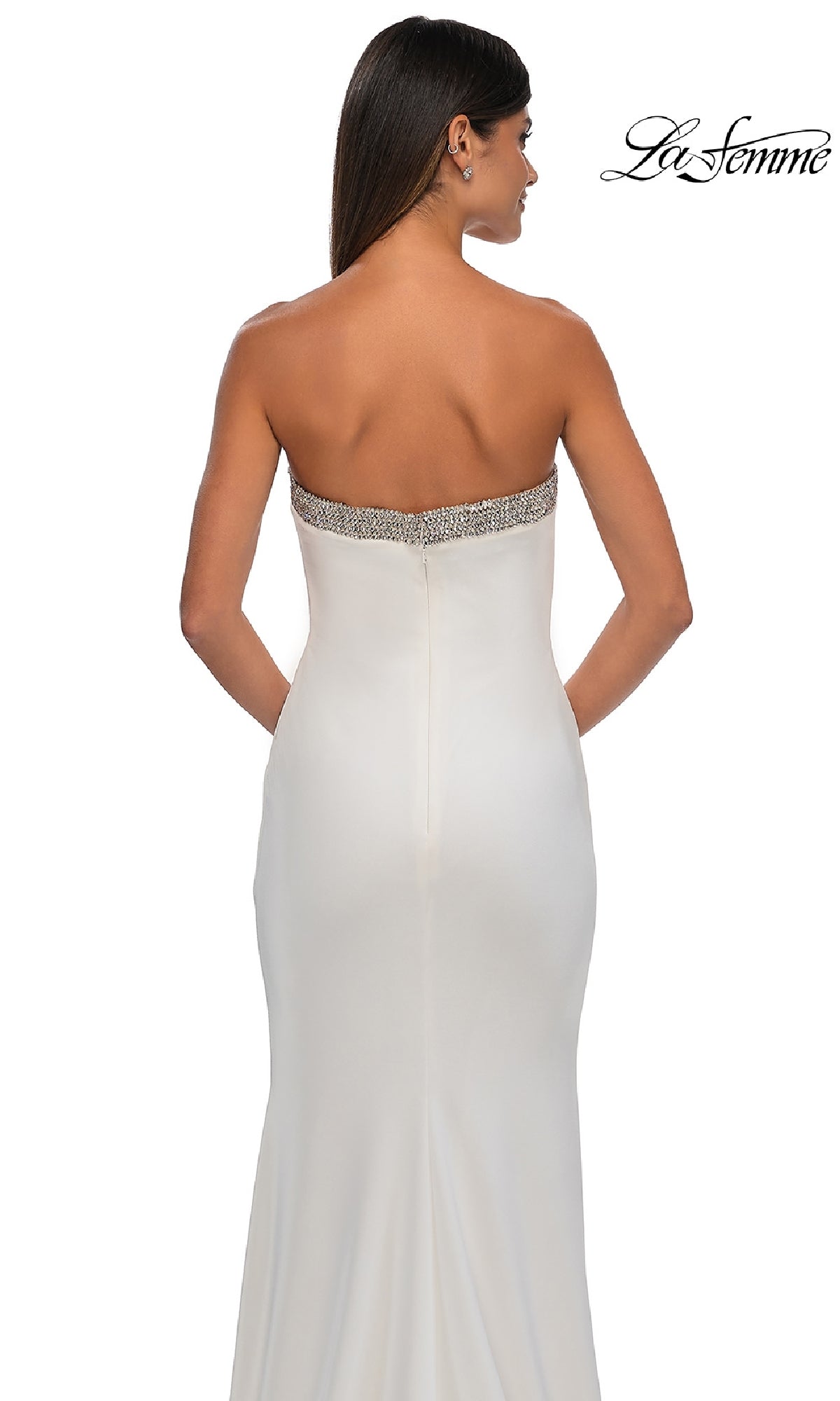 A woman faces away wearing the Bead-Trimmed Long Prom Dress: La Femme 32891, a fitted white strapless gown with embellished trim along the top.